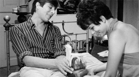 Schwarzweiß-Foto der Liebesszene aus dem Film "Zur Sache Schätzchen" mit Uschi Glas auf einem Bett sitzend zusammen mit Werner Enke beim Abspielen von einem Daumenkino