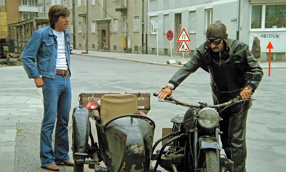 Werner Enke und Henry van Lyck in einer Szene im Kinofilm Hau drauf, Kleiner " (1974) bei ihrem Motorrad mit Beiwagen und dem Wort Heiduk im Hintergrund auf einer Hauswand stehend