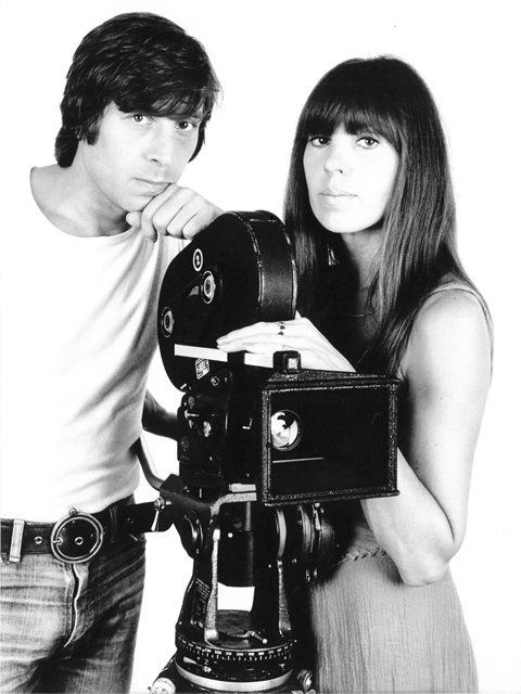 Schwarzweiß-Foto von Schauspieler Werner Enke und Regisseurin May Spils Mitte der 1970er Jahre, zwischen ihnen stehend eine analoge Arri-Filmkamera